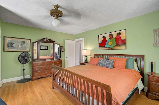 bedroom with light wood-style floors, baseboards, and a textured ceiling