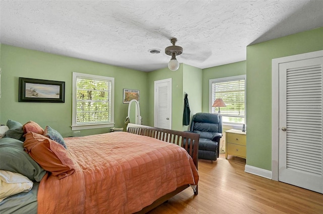 bedroom with visible vents, a ceiling fan, wood finished floors, a textured ceiling, and multiple closets