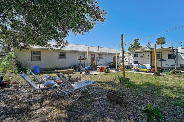 rear view of property with metal roof, a patio area, and a lawn