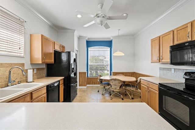 kitchen with a sink, light countertops, wainscoting, black appliances, and pendant lighting