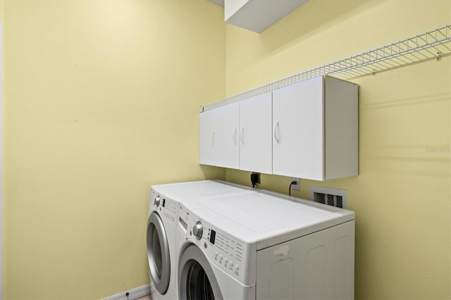 washroom featuring separate washer and dryer, cabinet space, and baseboards