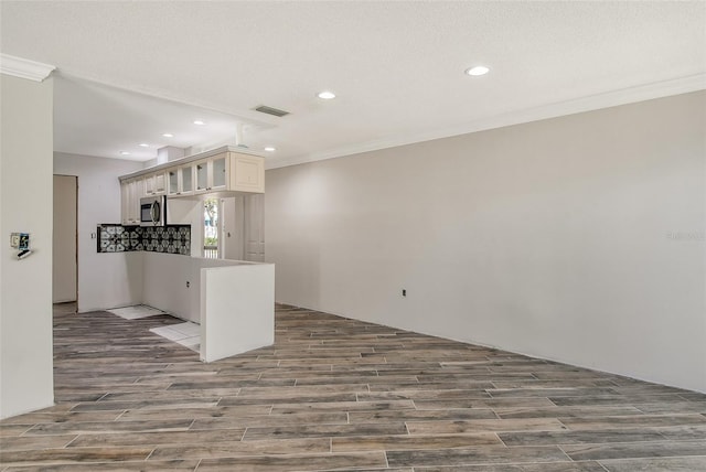 kitchen with visible vents, glass insert cabinets, stainless steel microwave, wood finished floors, and ornamental molding