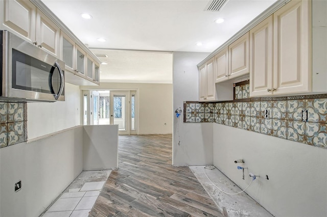 kitchen featuring cream cabinets, visible vents, light wood finished floors, stainless steel microwave, and glass insert cabinets