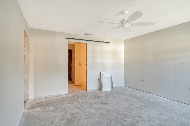 unfurnished room with a barn door, visible vents, unfinished concrete flooring, a ceiling fan, and a textured ceiling