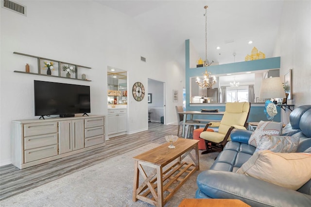 living room featuring an inviting chandelier, a towering ceiling, and light wood-type flooring