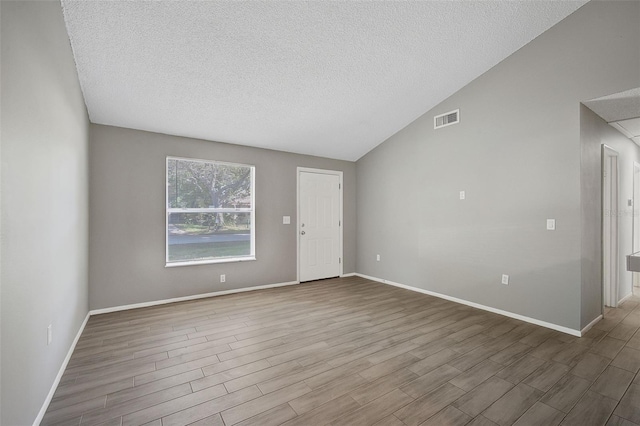 empty room featuring vaulted ceiling, wood-type flooring, and a textured ceiling