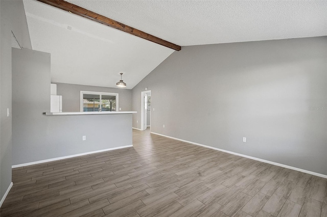 unfurnished living room with vaulted ceiling with beams, hardwood / wood-style floors, and a textured ceiling