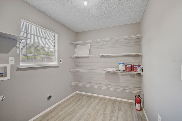 washroom featuring hookup for a washing machine, light hardwood / wood-style flooring, hookup for an electric dryer, and a textured ceiling