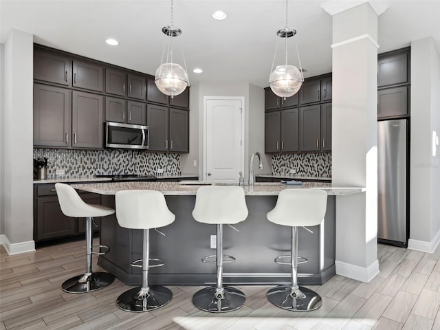 kitchen with a breakfast bar area, dark brown cabinets, a center island with sink, appliances with stainless steel finishes, and pendant lighting