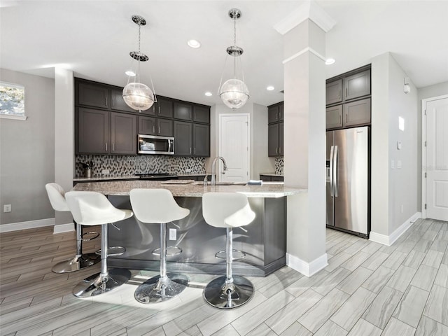 kitchen featuring sink, tasteful backsplash, light stone counters, hanging light fixtures, and stainless steel appliances