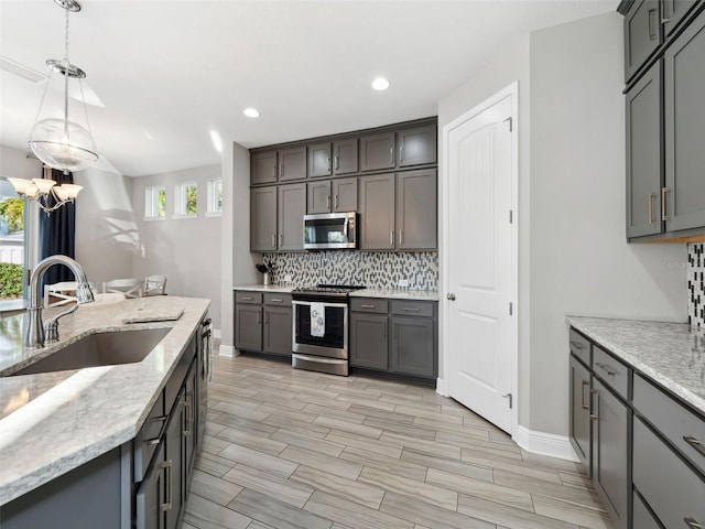 kitchen with sink, gray cabinetry, stainless steel appliances, decorative backsplash, and decorative light fixtures