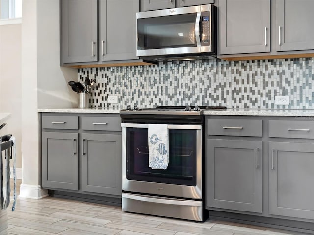 kitchen with gray cabinetry, backsplash, light stone counters, and stainless steel appliances