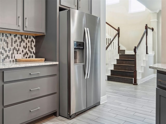 kitchen with light stone counters, light hardwood / wood-style flooring, stainless steel fridge, gray cabinets, and backsplash