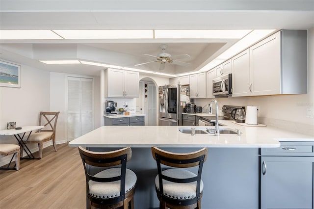 kitchen with appliances with stainless steel finishes, a breakfast bar, ceiling fan, kitchen peninsula, and light wood-type flooring