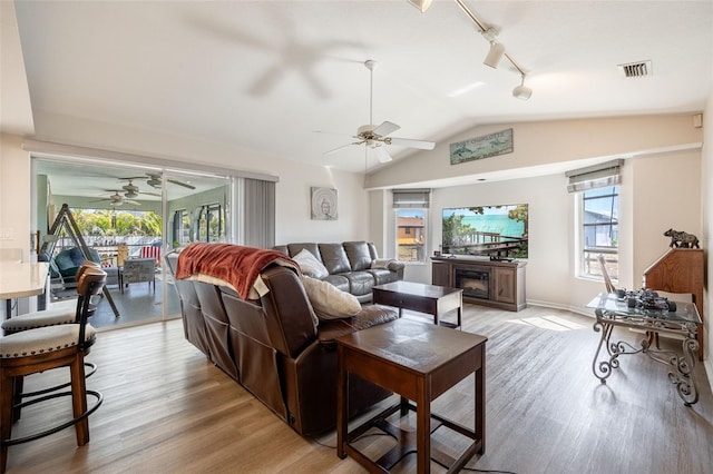 living room with lofted ceiling, rail lighting, light wood-type flooring, ceiling fan, and a fireplace