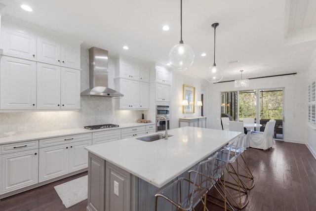 kitchen featuring sink, an island with sink, white cabinets, and wall chimney exhaust hood