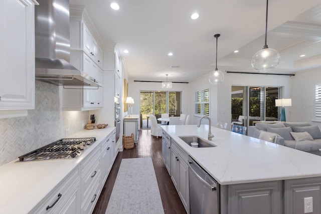 kitchen featuring sink, hanging light fixtures, a kitchen island with sink, stainless steel appliances, and wall chimney exhaust hood