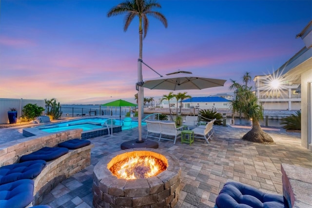 patio terrace at dusk with a fenced in pool and an outdoor fire pit