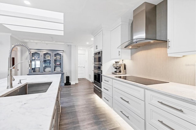 kitchen with black electric stovetop, sink, wall chimney range hood, and white cabinets