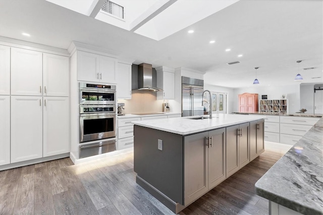 kitchen featuring white cabinets, wall chimney exhaust hood, light stone counters, stainless steel appliances, and a spacious island