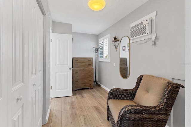 sitting room with a wall unit AC and light hardwood / wood-style flooring