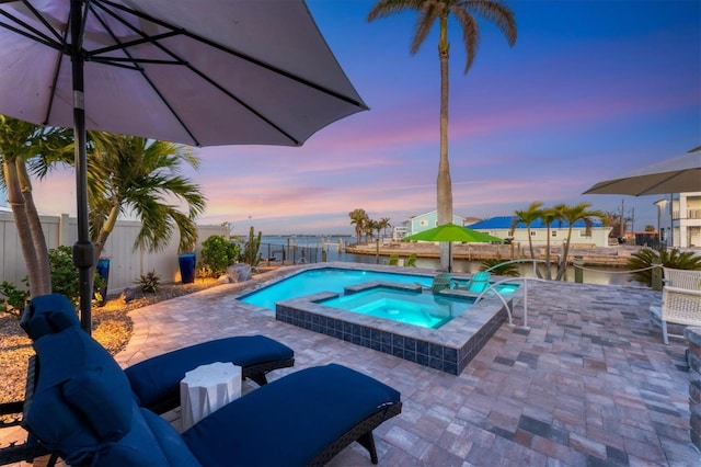 pool at dusk featuring an in ground hot tub and a patio area