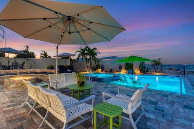 pool at dusk featuring a patio area, an outdoor living space with a fire pit, and an in ground hot tub