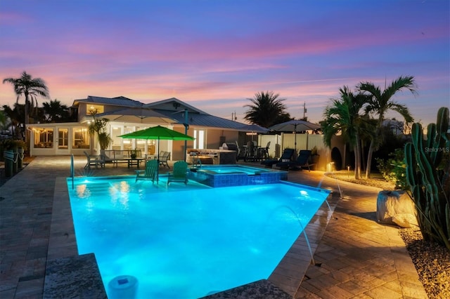 pool at dusk with an in ground hot tub, pool water feature, and a patio