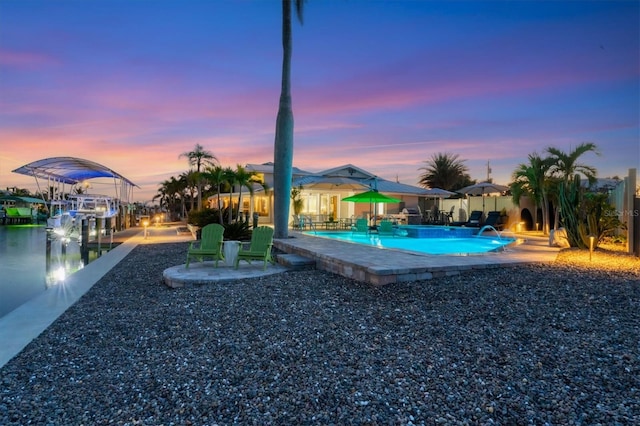 pool at dusk with a patio area, a boat dock, and a water view