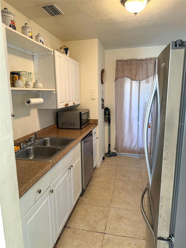 kitchen with light tile patterned flooring, appliances with stainless steel finishes, white cabinetry, sink, and a textured ceiling