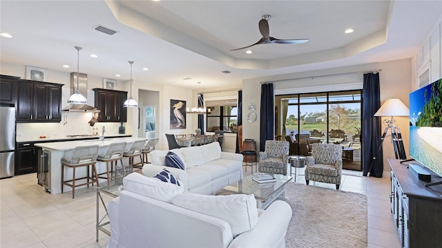 living room with ceiling fan with notable chandelier, a raised ceiling, and light tile patterned flooring