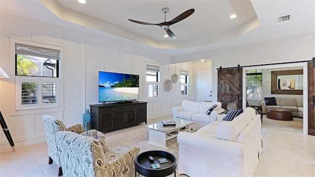 tiled living room featuring ceiling fan, a tray ceiling, and a barn door