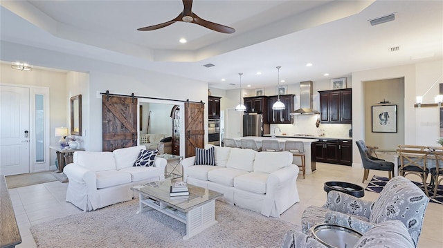 living room featuring sink, light tile patterned floors, ceiling fan, a tray ceiling, and a barn door