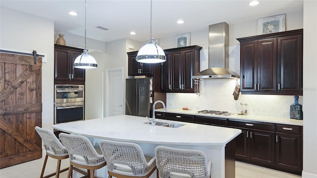 kitchen featuring wall chimney range hood, sink, appliances with stainless steel finishes, hanging light fixtures, and a barn door