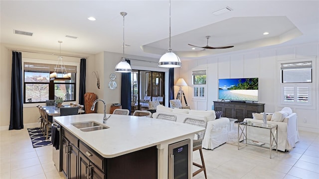 kitchen featuring sink, a breakfast bar area, hanging light fixtures, an island with sink, and beverage cooler