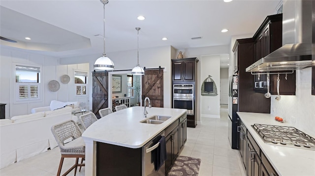 kitchen featuring a breakfast bar, a center island with sink, pendant lighting, a barn door, and wall chimney range hood