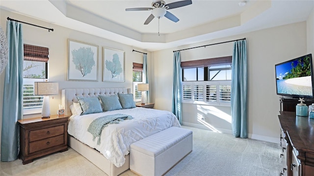 bedroom with light colored carpet, ceiling fan, and a tray ceiling