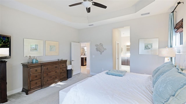 carpeted bedroom featuring connected bathroom, a tray ceiling, and ceiling fan