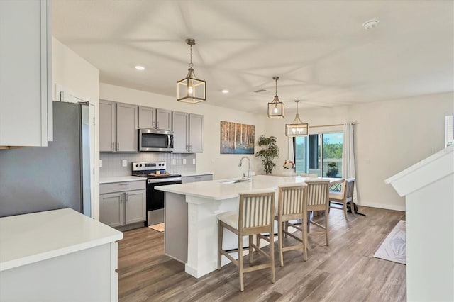 kitchen with gray cabinets, appliances with stainless steel finishes, backsplash, a center island with sink, and decorative light fixtures