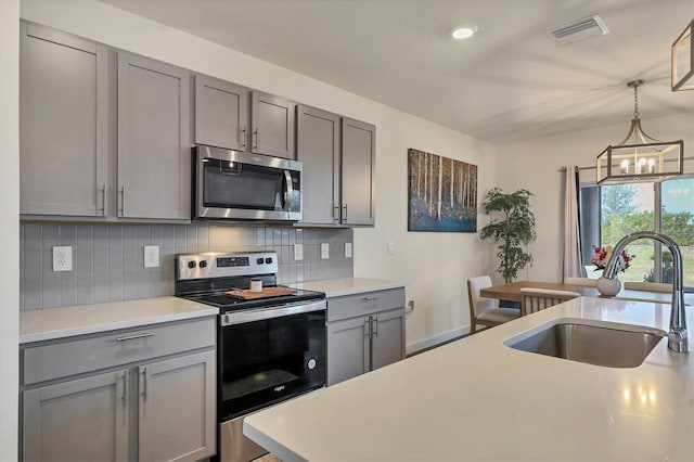 kitchen with pendant lighting, sink, gray cabinetry, decorative backsplash, and stainless steel appliances