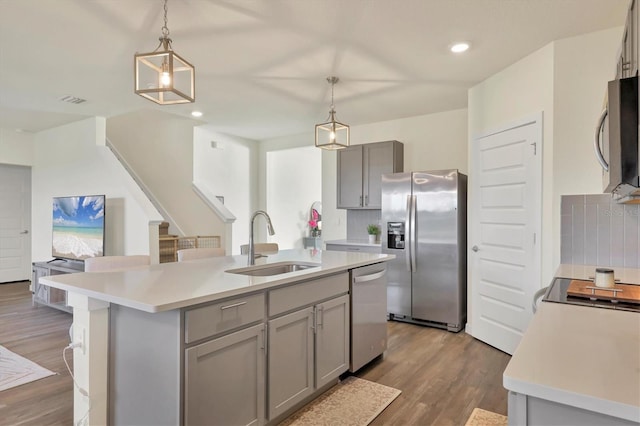 kitchen featuring gray cabinets, decorative light fixtures, sink, stainless steel appliances, and a center island with sink