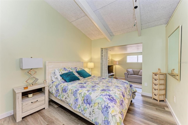 bedroom with wood-type flooring, lofted ceiling with beams, and a textured ceiling