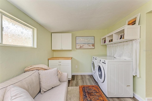 clothes washing area with washing machine and dryer, cabinets, a textured ceiling, and light wood-type flooring