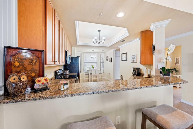 kitchen with appliances with stainless steel finishes, a tray ceiling, kitchen peninsula, and a notable chandelier