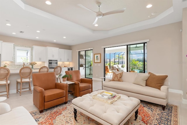 living room featuring ceiling fan, a raised ceiling, and light tile patterned floors