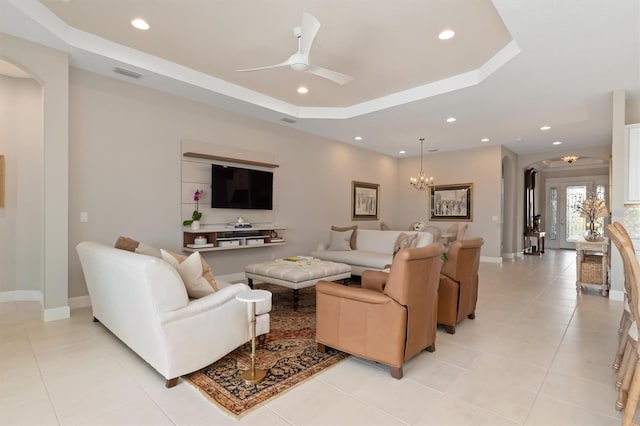 tiled living room with a raised ceiling and ceiling fan with notable chandelier