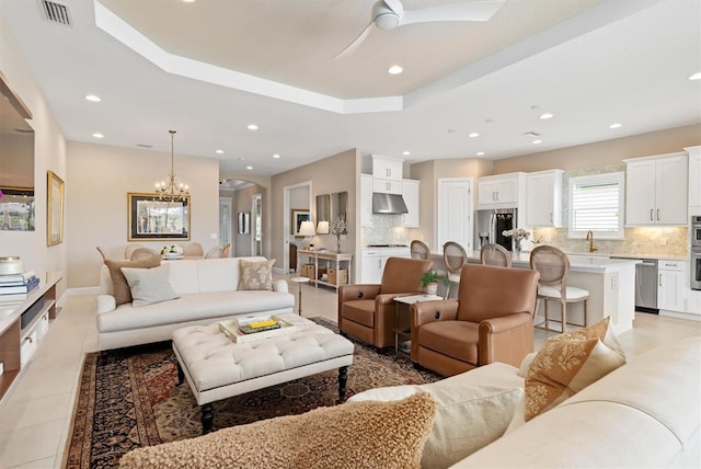 living room featuring ceiling fan with notable chandelier, a raised ceiling, and light tile patterned flooring