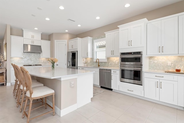 kitchen with a kitchen island, appliances with stainless steel finishes, white cabinetry, a kitchen breakfast bar, and light tile patterned floors