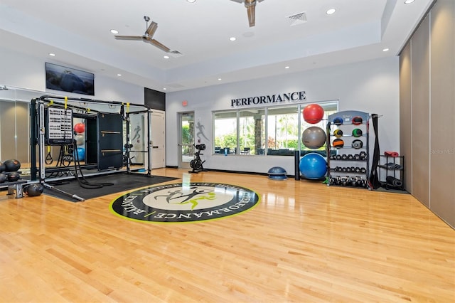 workout area with hardwood / wood-style flooring, ceiling fan, and a tray ceiling