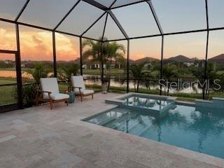 pool at dusk with an in ground hot tub, a patio, and glass enclosure